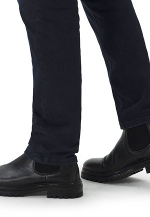 Schwarze Lederknöchelboots mit strukturierten Akzenten und Mesh-Panels, kombiniert mit dunkelblauen schmal geschnittenen Hosen, die eine Seitenansicht zeigen.