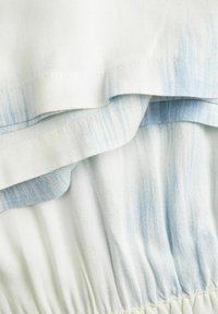 Baltas audinys su šviesiai mėlynomis juostomis, turintis susiraukšlėjusį raštą ir sluoksniuotas volanėles. Siuvinėtos briaunos ir švelnus, lygus paviršius.