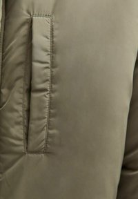 Giacca isolante verde oliva con un motivo a righe orizzontali, una tasca laterale e un tessuto liscio e resistente all'acqua.
