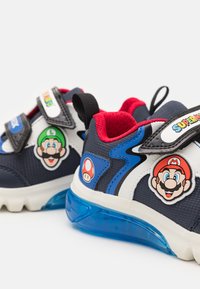 Kék sportcipők piros kiegészítőkkel, Mario és Luigi mintával. Hálós és szintetikus anyagból készült, texturált felülettel és tépőzáras pántokkal.