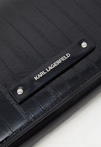 Fekete bőrtárca texturált felülettel, ezüst logós táblával és patentos részlettel. Simább, téglalap alakú, sima felülettel.