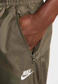 Nike krátké kalhoty v olivově zelené barvě, s kapsou na zip a bílým logem. Materiál působí lehce a hladce, s matným finišem.