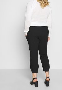 Czarne spodnie zwężane z elastycznymi mankietami, zestawione z białym, dzianym topem. Top ma luźny krój i fakturowany wzór.