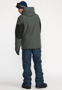 Gray and black waterproof jacket with a hood, paired with blue snow pants. Features a relaxed fit and textured fabric for insulation and comfort.