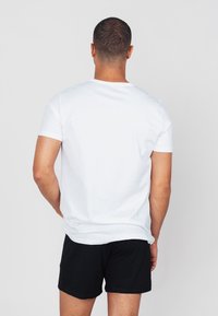 Weißes T-Shirt mit kurzen Ärmeln und Rundhalsausschnitt, entspannter Schnitt, kombiniert mit schwarzen Shorts. Minimalistisches Design ohne sichtbare Logos oder Muster.
