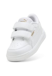Sneakers bianche con una superficie liscia simile alla pelle, doppie fasce in Velcro, punta perforata e dettaglio dorato con logo sul lato. Forma della punta arrotondata.