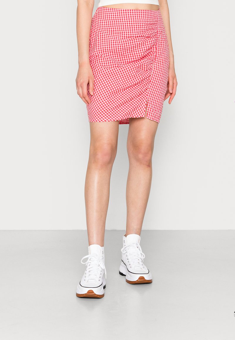 Saia mini xadrez em vermelho e branco com detalhes franzidos na frente, combinada com ténis brancos de cano alto. Textura suave.