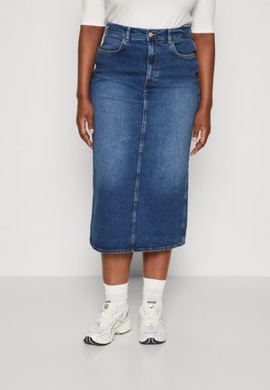 Niebieska, midi spódnica dżinsowa noszona z białymi trampkami, białymi skarpetkami i białą bluzką, pokazana od środkowej części tułowia do stóp.