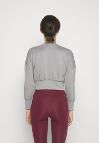 Felpa grigia corta con maniche oversize e orlo elastico, abbinata a leggings borgogna a vita alta, che mostrano una texture liscia.