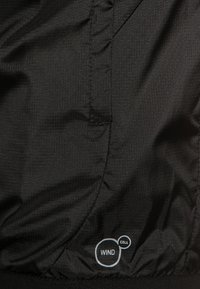 Black windbreaker jacket with a textured fabric, featuring a "WIND CELL" label in blue, designed for wind resistance and breathability.