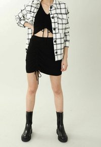Czarny krótki top z marszczonymi detalami, zestawiony z czarną marszczoną mini spódniczką z troczkami, noszony pod białą kratowaną kurtką.