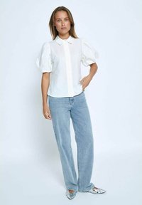Blusa bianca con maniche a sbuffo, colletto a punta e chiusura con bottoni, abbinata a jeans a gamba larga di un blu chiaro e scarpe argentate decorate.
