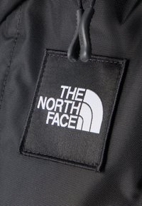 Μαύρο ετικέτα λογότυπου The North Face ραμμένη σε υφή μαύρου υφάσματος με κοντινά μαύρα κορδονάκια φερμουάρ.