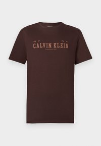 Tamno smeđa pamučna majica s logotipom "CALVIN KLEIN" u svjetlijoj smeđoj boji. Kratki rukavi, okrugli izrez i ravni rub. Jednostavan dizajn.