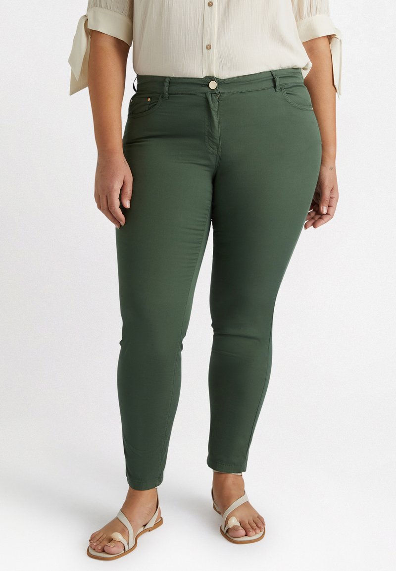 Jean vert, slim fit, avec une texture lisse, présentant des poches avant et une fermeture à bouton, associé à une chemise légère à manches courtes.