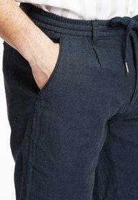 Námořnické modré kalhoty s herringbone vzorem, s elastickým pasem na šňůrku, postranními kapsami a texturovanou tkaninou, s volným střihem a pevným švem.