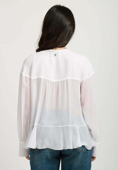 Blusa bianca e trasparente con maniche lunghe, schiena plissè e orlo a strati. Presenta un semplice collo rotondo e un branding discreto sul retro.