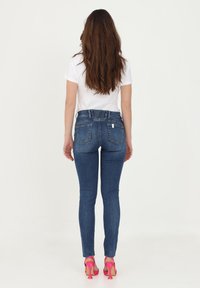 Jeans de mezclilla azul de cintura alta con un ligero estiramiento, que presentan una cintura trasera fruncida, y combinados con sandalias de tacón de color rosa brillante.
