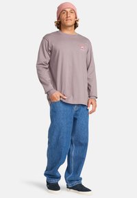 Długopisowa bluzka w kolorze mauve z logo na piersi, niebieskie luźne dżinsy i różowa, żeberkowana czapka. Swobodny wygląd z luźnym krojem i miękką teksturą.