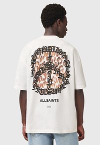 Hvid oversized t-shirt med et leopardmønstret fredstegn-design og sort tekst på bagsiden. Casual pasform og korte ærmer.