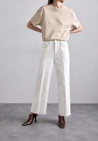 Camiseta de algodón color beige, de corte relajado. Jeans de tiro alto blancos de pierna ancha con dobladillo deshilachado. Botines de tacón marrón oscuro con punta afilada.