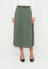 Πράσινη μίντι φούστα από απαλό ύφασμα, με ελαστική μέση και καφέ ζώνη. Συνδυασμένη με μαύρες γόβες με μυτερή μύτη.