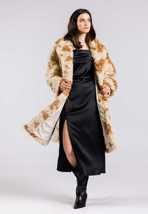 Manteau en fausse fourrure avec des motifs orange et crème, coupe oversize, associé à une robe en satin noire élégante avec une fente haute sur la cuisse et des bottes noires.