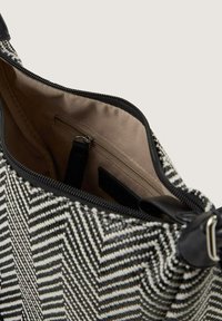 Zwart-wit chevronpatroon stoffen tas met een ritsafsluiting; heeft een beige interieur met een ritsvak en zwarte leren accenten.