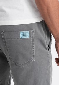 Grijze denim broek met een achterzak voorzien van een lichtblauwe 'ombre denim' label. De stof is zacht en heeft een licht vervaagde textuur.