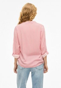 Chemise rayée rouge et blanche avec des manches retroussées, en tissu léger, et un détail de dos avec empiècement, associée à un jean bleu.