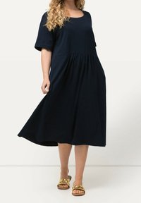 Sinihimmed midi-mekko pehmeästä kankaasta, jossa on lyhyet hihat, pyöreä pääntie ja kerätty vyötärö, yhdistettynä kultaisiin liukuvaan sandaaleihin.