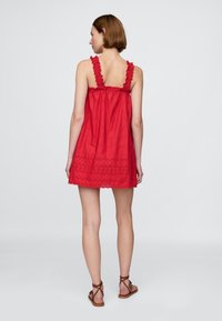 Vörös ujjatlan ruha fodros pántokkal, csipke díszítéssel és hímzett virágmintával. Könnyű anyagból készült, kényelmes, bővülő sziluettel.