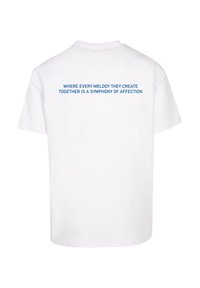 Biela bavlnená tričko s modrým textom na chrbte, ktorý znie: "KDE KAŽDÁ MELODIA, KTORÚ SPOLU TVORIA, JE SYMFÓNIOU NÁKLONNOSTI."