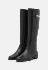 Botas negras hasta la rodilla, fabricadas en cuero suave, con un sutil acento en metal dorado y punta redondeada. Textura uniforme, diseño minimalista.