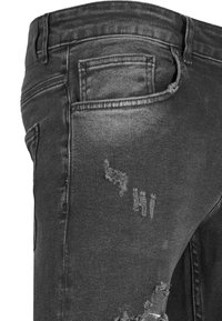 Jeans de mezclilla negra con corte slim, que presentan detalles desteñidos, un bolsillo trasero y un sutil desgaste, enfatizando la textura de la tela.
