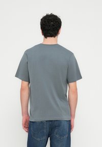 Szürke pamutpóló kerek nyakkivágással és rövid ujjakkal, sima textúrával és laza szabással, hátulnézetben.