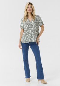 Blusa floreale a maniche corte verde con fiori bianchi, abbinata a jeans blu a gamba dritta e décolleté beige a punta.