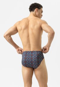 Zwemslips in marineblauw met een geometrisch patroon en rode en blauwe accenten. Gemaakt van rekbaar materiaal voor comfort en pasvorm.