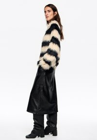 Nepbont gestreepte trui in cream en zwart, gecombineerd met een zwarte leren maxi-rok en zwarte laarzen tot de knie.