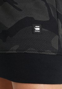 Mustat urheilushortsit, joissa on teksturoitu, camouflage-kuvio. Yksityiskohtana ribattu resori ja pieni musta etiketti "RAW"-logolla helmassa.