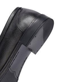 Chaussure en cuir noir avec une texture lisse, un embout arrondi et une semelle en caoutchouc flexible. Présente des accents cousus et un talon robuste.