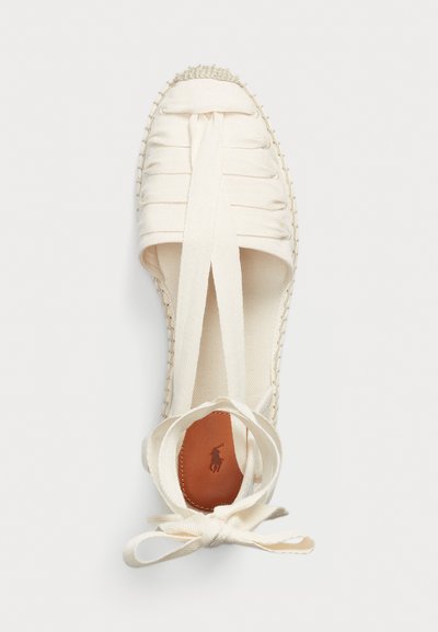 Espadrille blanca con parte superior de lienzo, suela de yute trenzado, tiras de tela cruzadas, puntera redonda y un borde trenzado reforzado en la punta.
