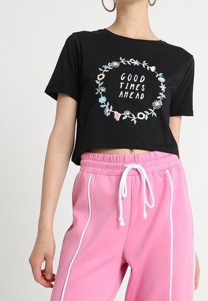 Czarny krótki t-shirt z kwiatowym nadrukiem i napisem "GOOD TIMES AHEAD", zestawiony z różowymi dresowymi spodniami z białymi bocznymi paskami.
