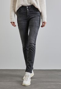 Służące slim-fit czarne dżinsy z przednimi kieszeniami i wyblakłą teksturą, połączone z białymi trampkami i lekkim swetrem.