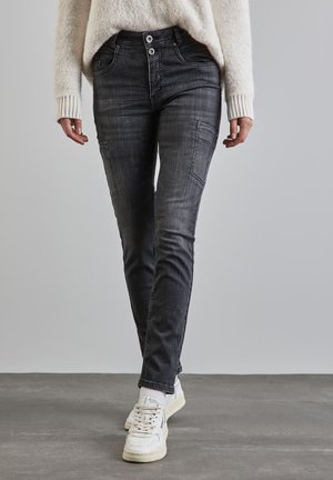 Jeans en denim noir slim avec poches avant et texture délavée, associés à des baskets blanches et un pull léger.