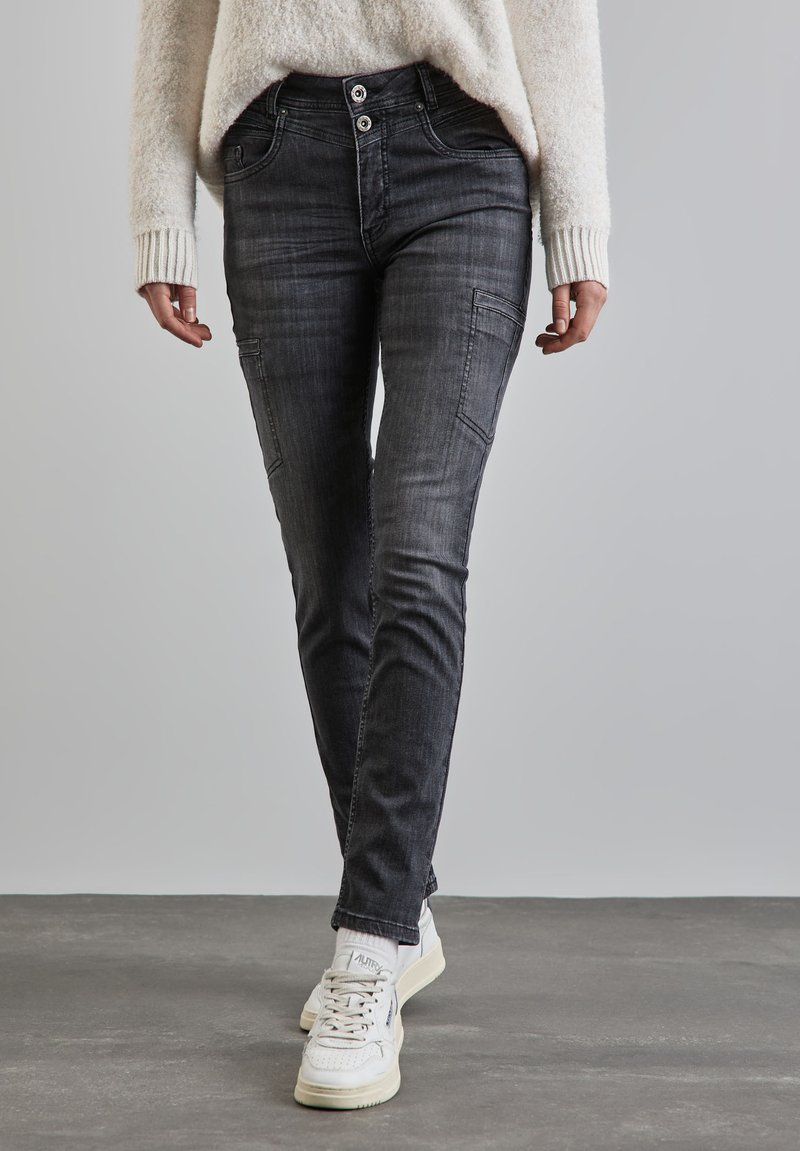 Służące slim-fit czarne dżinsy z przednimi kieszeniami i wyblakłą teksturą, połączone z białymi trampkami i lekkim swetrem.