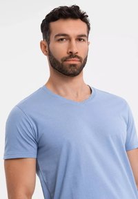 Světle modré tričko s výstřihem do V vyrobené z měkké bavlny, s krátkými rukávy a hladkou texturou, těsně přiléhající k trupu.