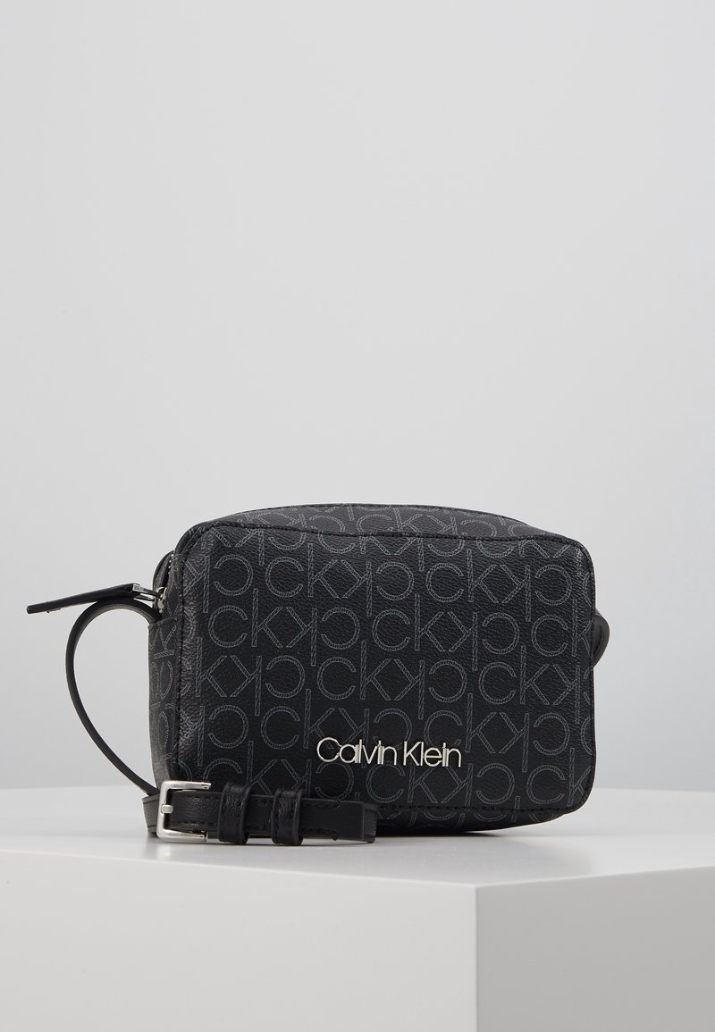 Czarna skórzana torebka na ramię z logo Calvin Klein, z powtarzającym się wzorem i srebrnymi akcentami. Kompaktowy prostokątny kształt.