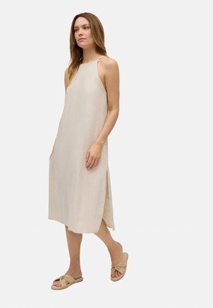 Vestido midi de lino en color beige claro, con tirantes finos, aberturas laterales y una silueta relajada. Combinado con sandalias de tiras anudadas.