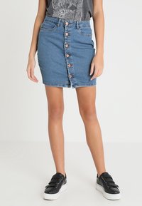 Denimová sukně s předním zapínáním na knoflíky, světle modrá barva, přiléhavý střih, pět kapes a surový lem. V kombinaci s černými teniskami.